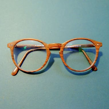 Close-up of fashionable wooden frame eyeglasses on a solid blue background.