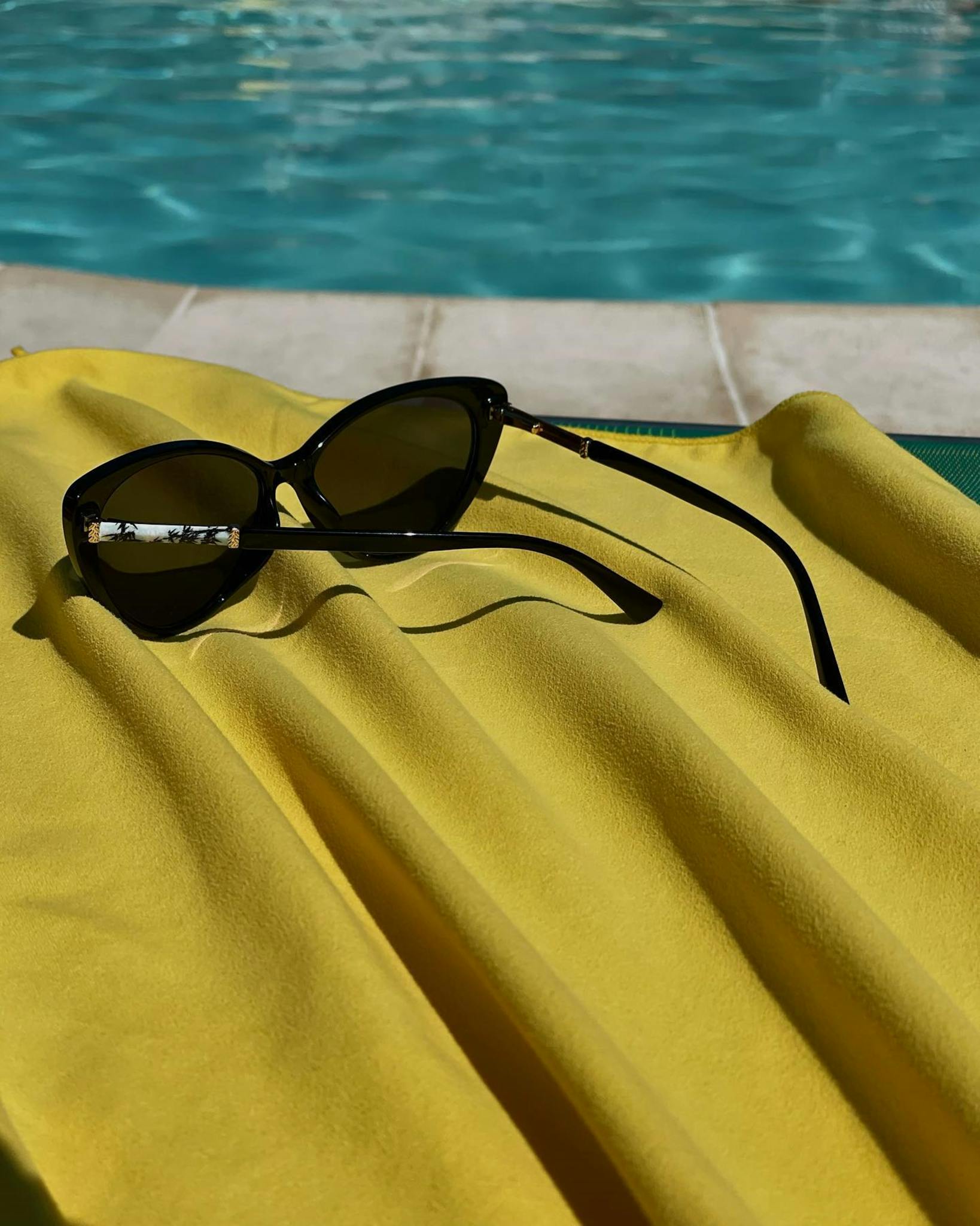 Stylish sunglasses resting on a vibrant yellow towel by a pool, capturing a relaxing summer vibe.