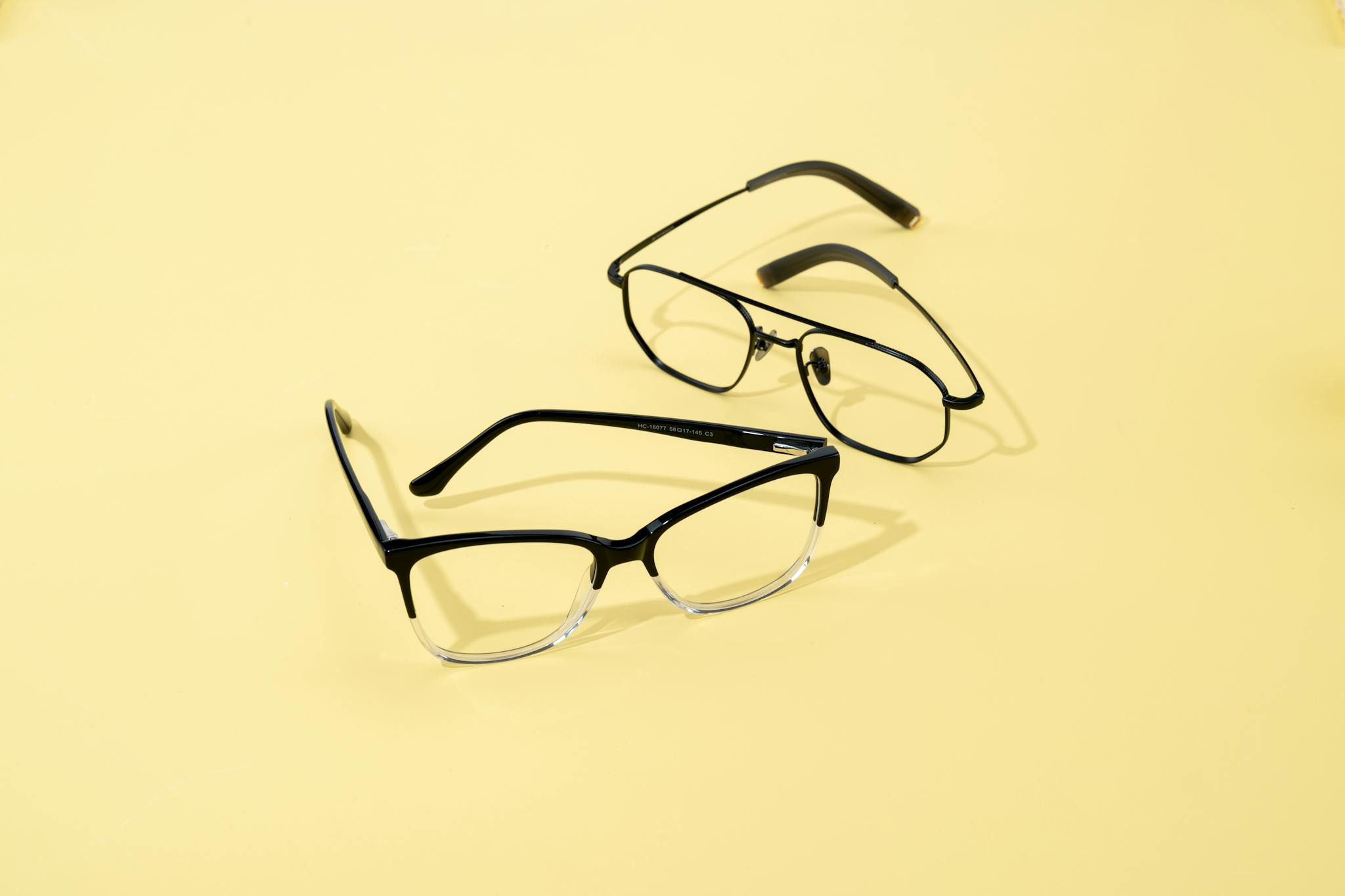 Two pairs of fashionable eyeglasses on a minimalist yellow backdrop.